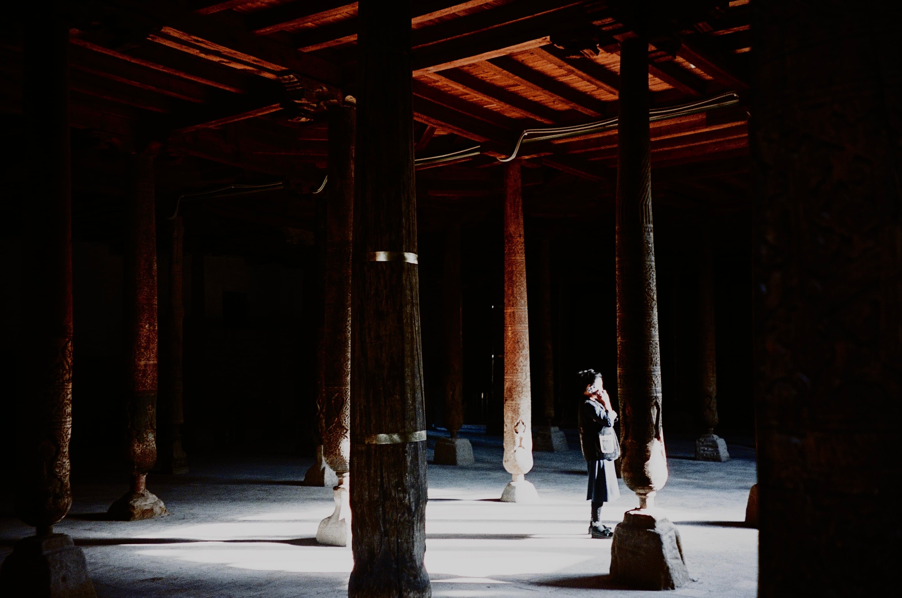 A dark hall of carved wooden columns, a figure standing in the light
