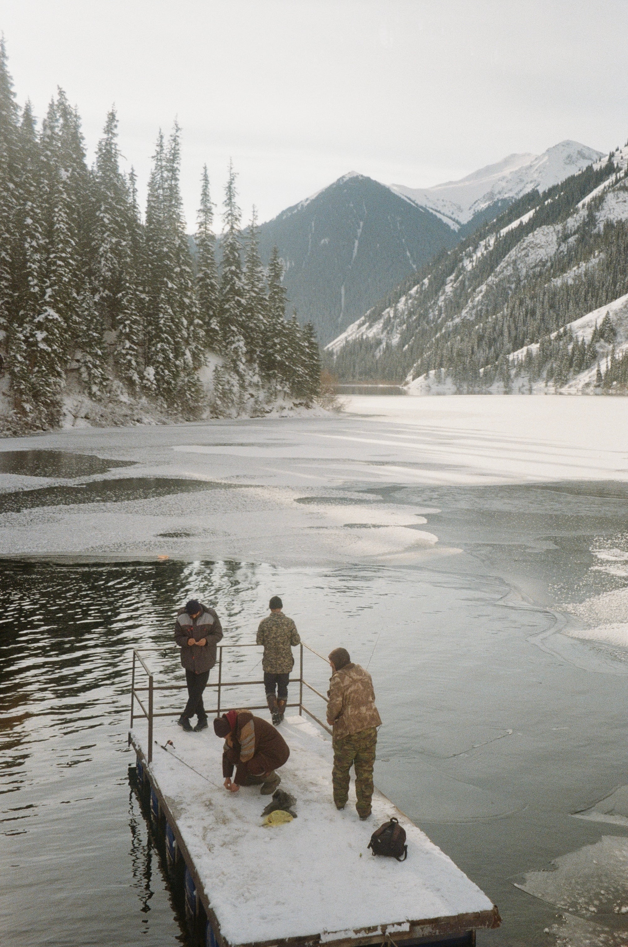 Figures on a wooden jetty over a frozen mountain lake