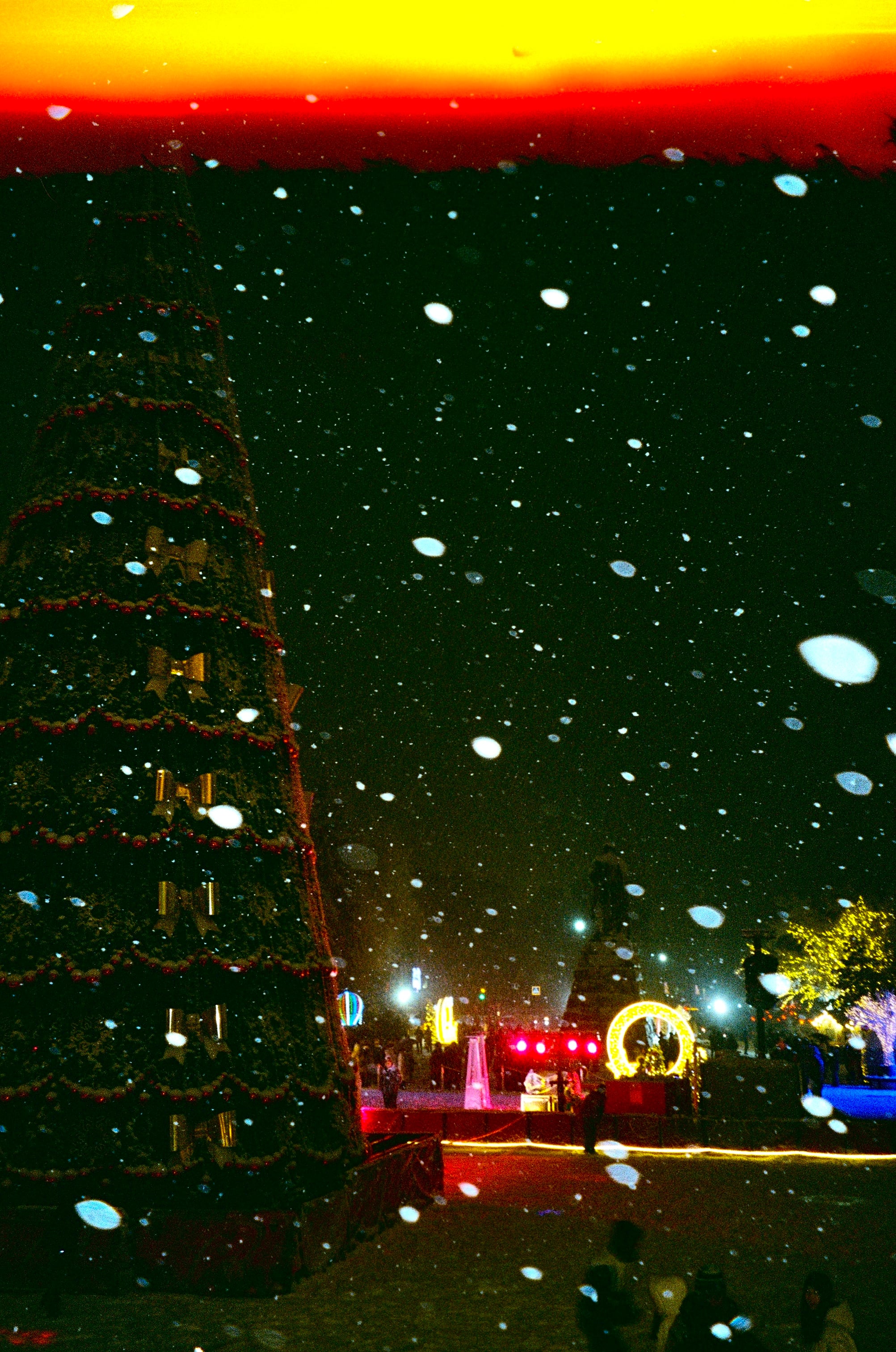 Night lights through falling snow beneath an orange-lit sky