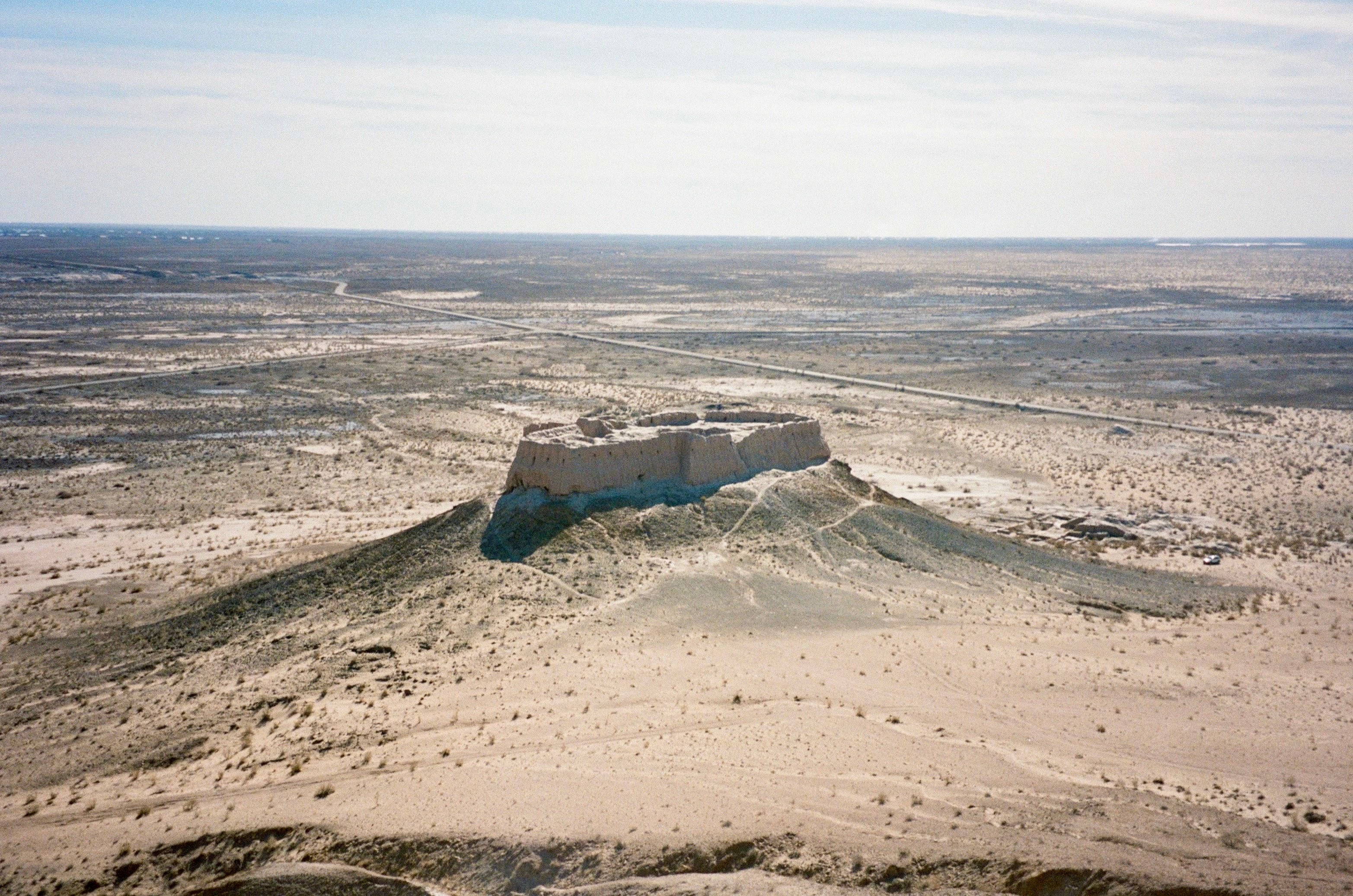 A desert plain seen from above, a ruined walled fort at its centre