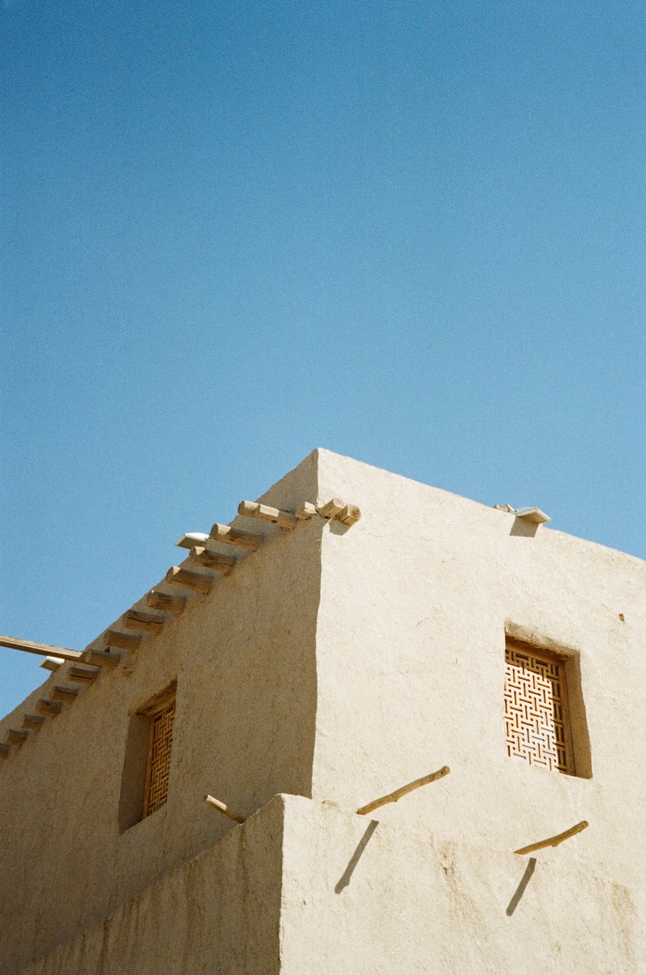 The sunlit corner of a mud-brick building against a blue sky